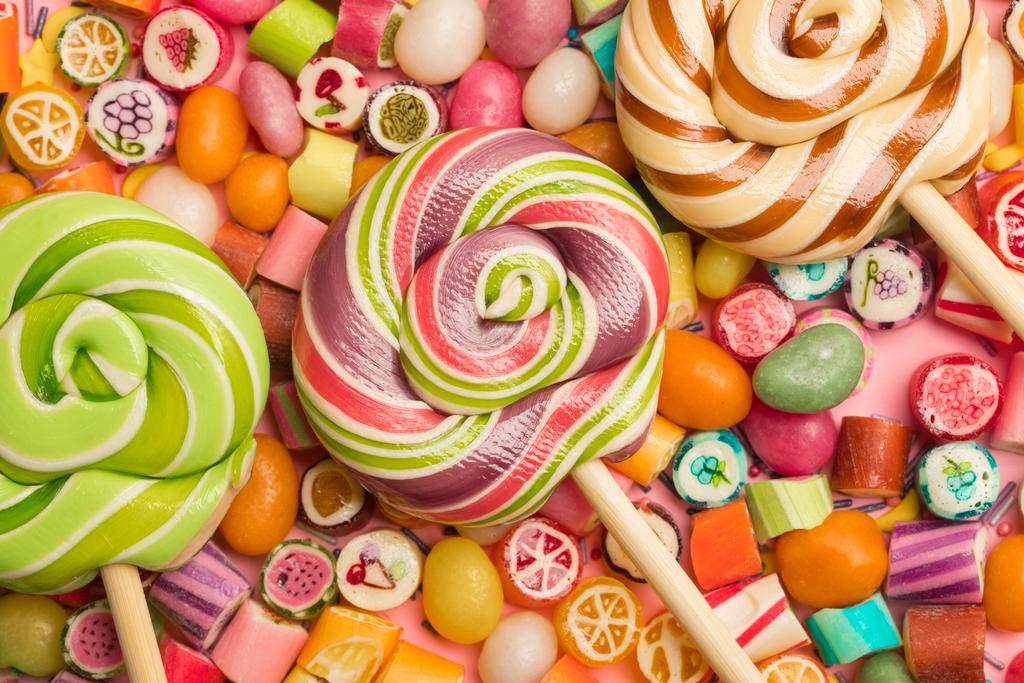 вид сверху на яркие вкусные разноцветные карамельные конфеты и леденцы на деревянных палочках
 - Фото, изображение
