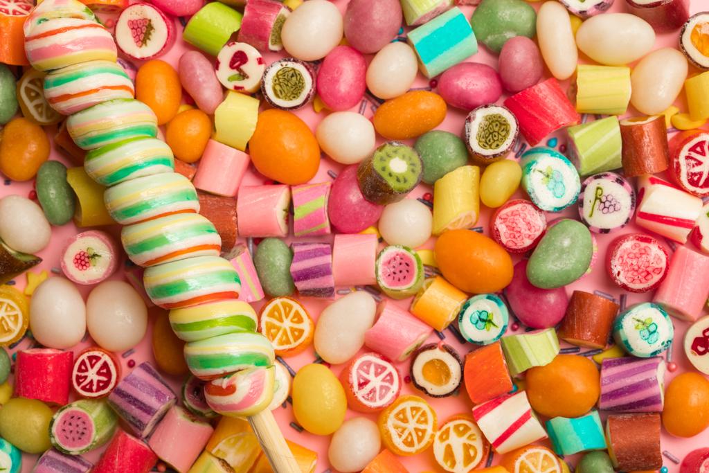 vista superior de brillantes deliciosos caramelos multicolores y piruleta remolino en palo de madera
 - Foto, imagen
