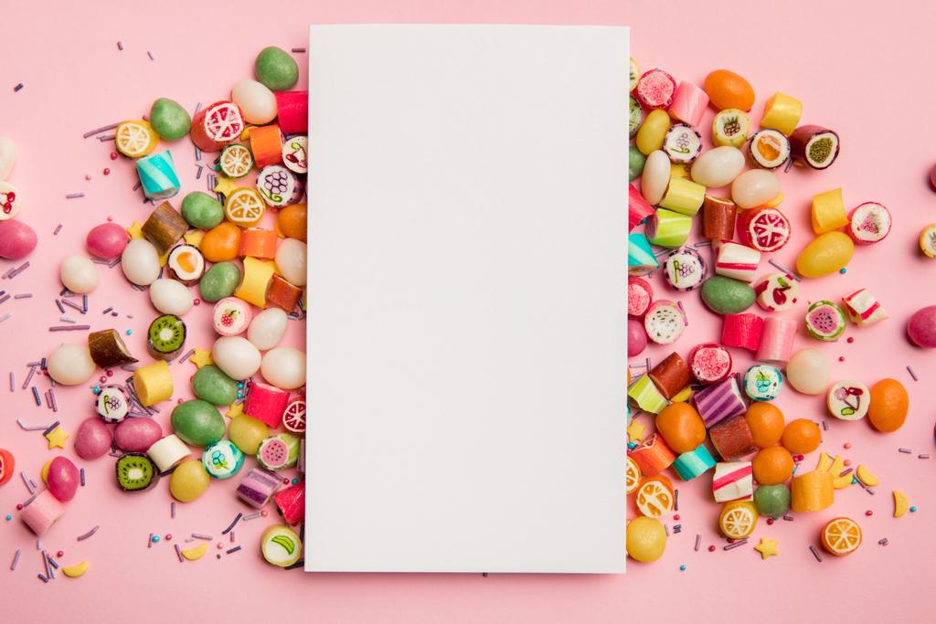 vista superior de deliciosos caramelos multicolores y tarjeta blanca con espacio de copia sobre fondo rosa
 - Foto, Imagen