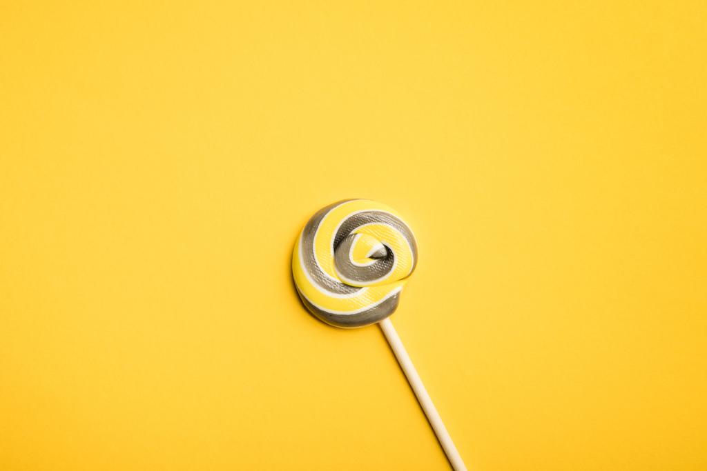 top view of delicious multicolored swirl lollipop on wooden stick on yellow background - Photo, Image