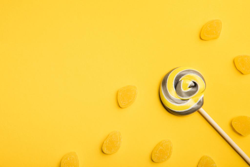 Top uitzicht van heerlijke veelkleurige Swirl Lollipop op houten stok en gelei op gele achtergrond - Foto, afbeelding