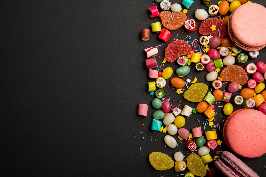 vista superior de deliciosos doces multicoloridos, polvilhas e macarons no fundo preto
  - Foto, Imagem