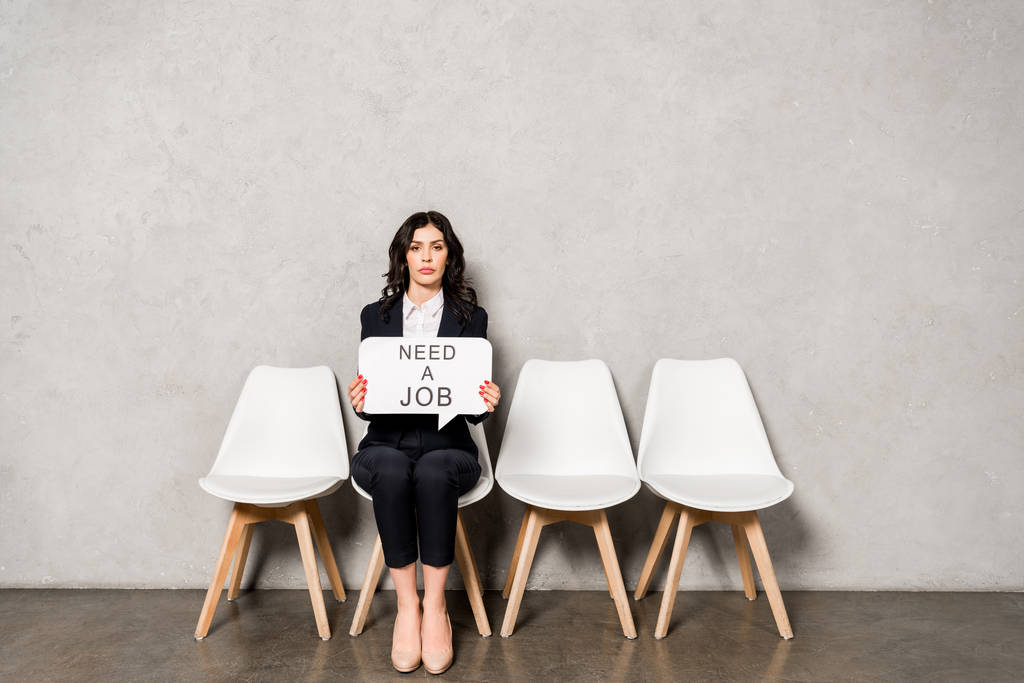attraktive brünette Frau mit Sprechblase, die einen Job-Schriftzug braucht, während sie auf dem Stuhl sitzt  - Foto, Bild