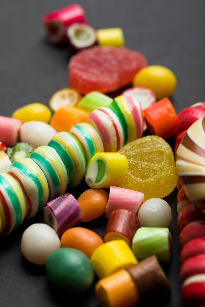 selectieve focus van heerlijke veelkleurige karamel en gelei snoepjes op zwarte achtergrond - Foto, afbeelding