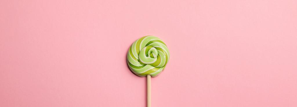 panoramische shot van groene ronde Lollipop op houten stok op roze achtergrond - Foto, afbeelding