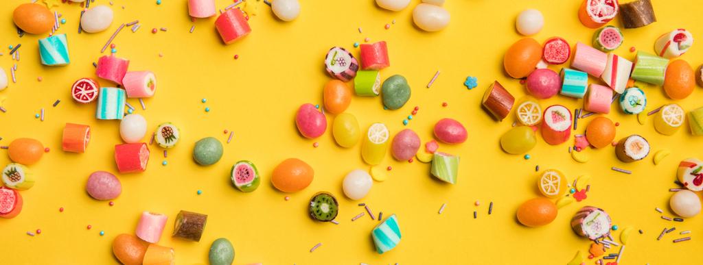 plano panorámico de caramelos multicolores y salpicaduras esparcidas sobre fondo amarillo
  - Foto, Imagen