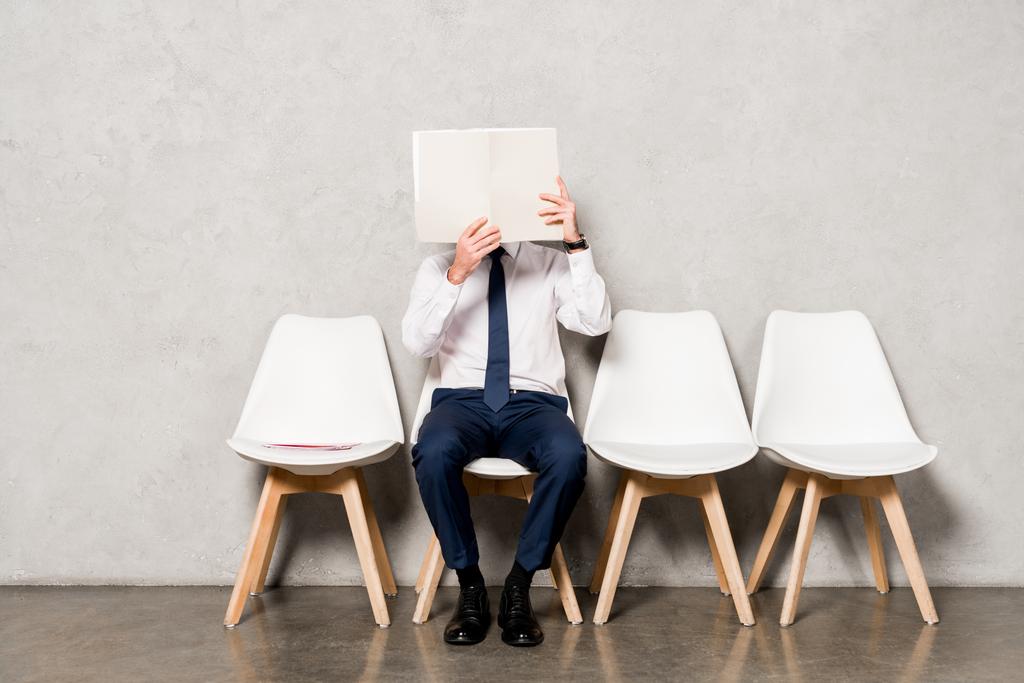 człowiek w formalnym nosić pokrycie twarzy z pustym papierem i siedzi na krześle  - Zdjęcie, obraz