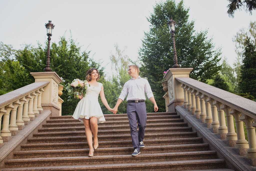 νεαρή νύφη και γαμπρός ποζάρουν σε τσιμεντένια μαρμάρινα σκαλοπάτια - Φωτογραφία, εικόνα