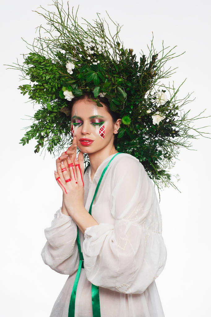 Retrato de uma mulher bonita em um vestido branco com uma fita verde e com ramos na cabeça. Maquiagem criativa
 - Foto, Imagem