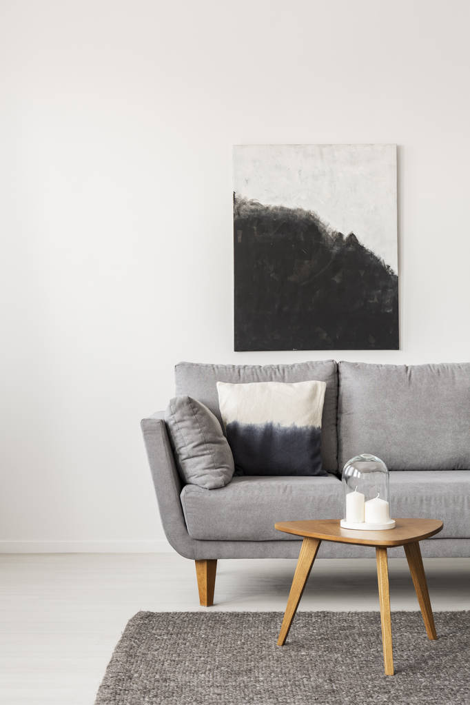 キャンドル付きの木製のコーヒーテーブルと枕付きの灰色のソファと空の白い壁に抽象的な黒と白の絵 - 写真・画像