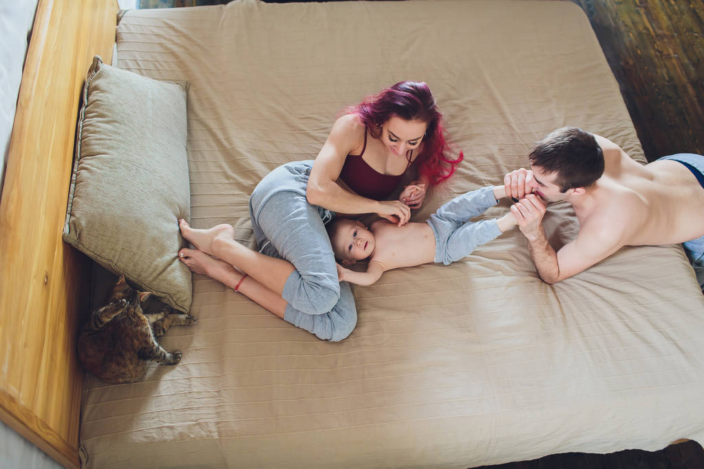 boldog fiatal szülők-val baba és macska az ágyban otthon. - Fotó, kép