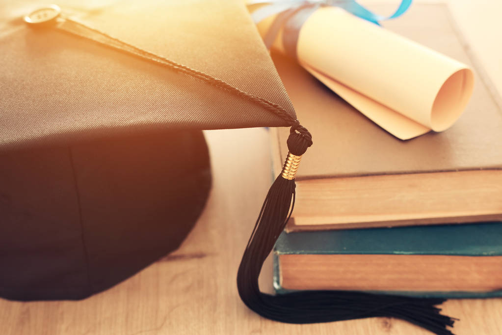 φωτογραφία της αποφοίτησης μαύρο καπέλο πάνω από παλιά βιβλία δίπλα στο δίπλωμα κύλισης στο ξύλινο γραφείο. Εκπαίδευση και επιστροφή στη σχολική έννοια - Φωτογραφία, εικόνα