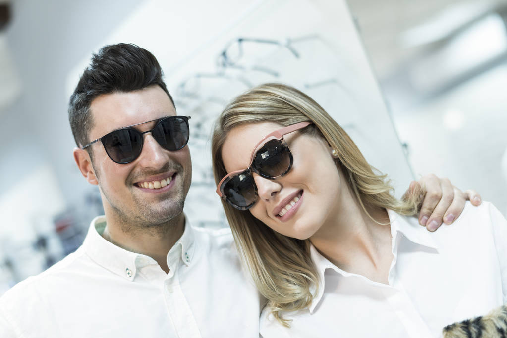 Пара з сонцезахисними окулярами посміхається і дивиться на камеру в магазині окулярів
 - Фото, зображення