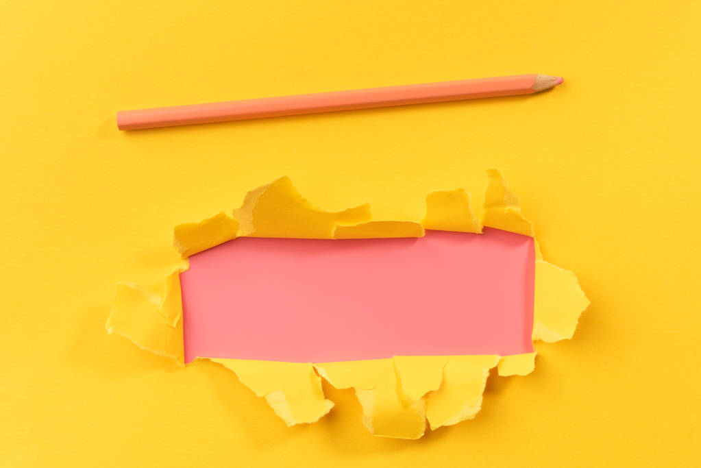 Geel gescheurd papier over roze achtergrond met potlood - Foto, afbeelding