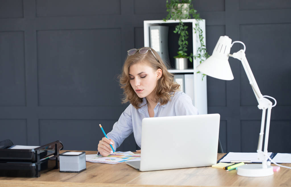 Концентрована молода красива бізнес-леді, що працює на ноутбуці в яскравому сучасному офісі
 - Фото, зображення
