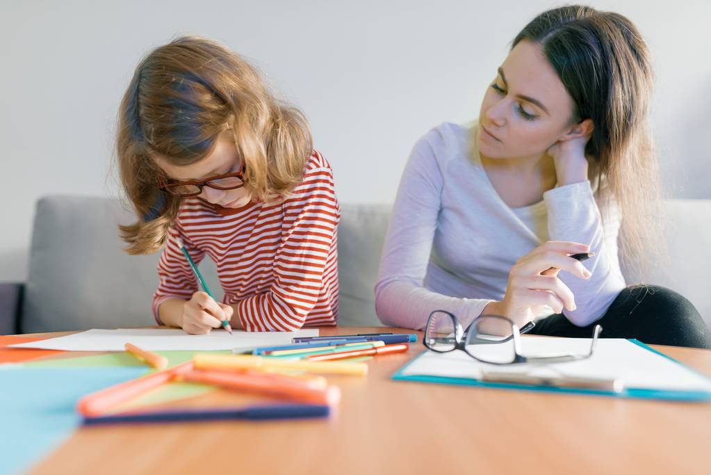 junge Lehrerin gibt Kind Privatunterricht, kleines Mädchen sitzt am Schreibtisch und schreibt in Notizbuch - Foto, Bild