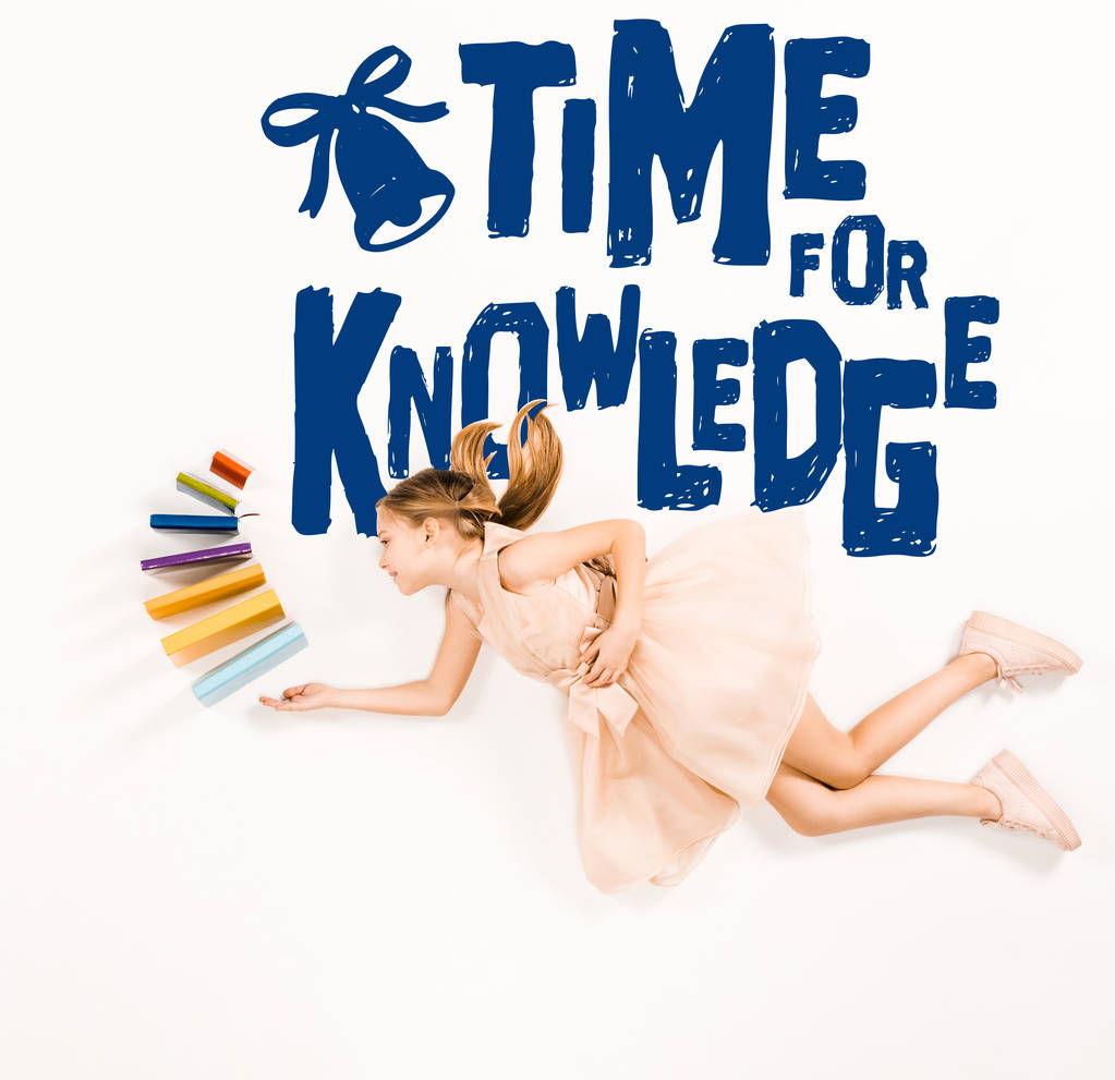 top view of cheerful kid in pink dress holding books and flying near time for knowledge lettering on white - Photo, Image