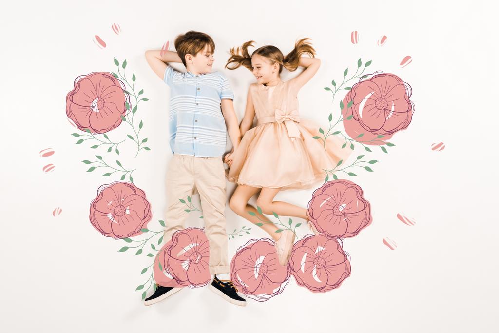 Blick von oben auf fröhliche Kinder, die sich in der Nähe rosafarbener Blumen an weißen Händen halten  - Foto, Bild