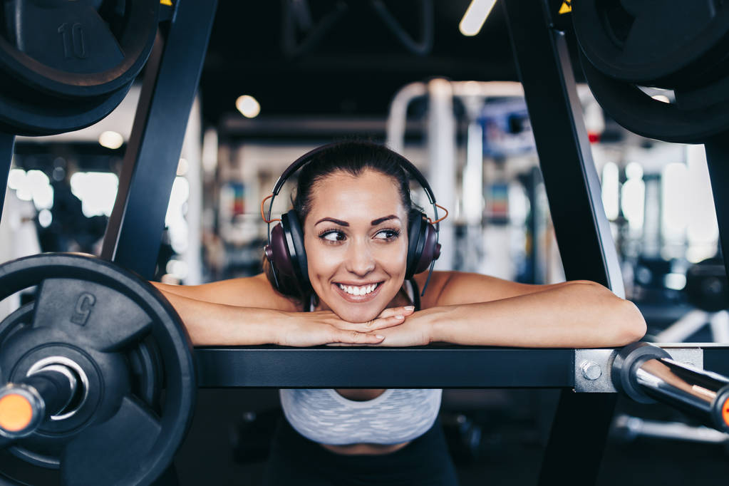 junge, fitte und attraktive Frau, die im modernen Fitnessstudio trainiert und mit Bluetooth-Kopfhörern und Smartphone Musik hört. - Foto, Bild