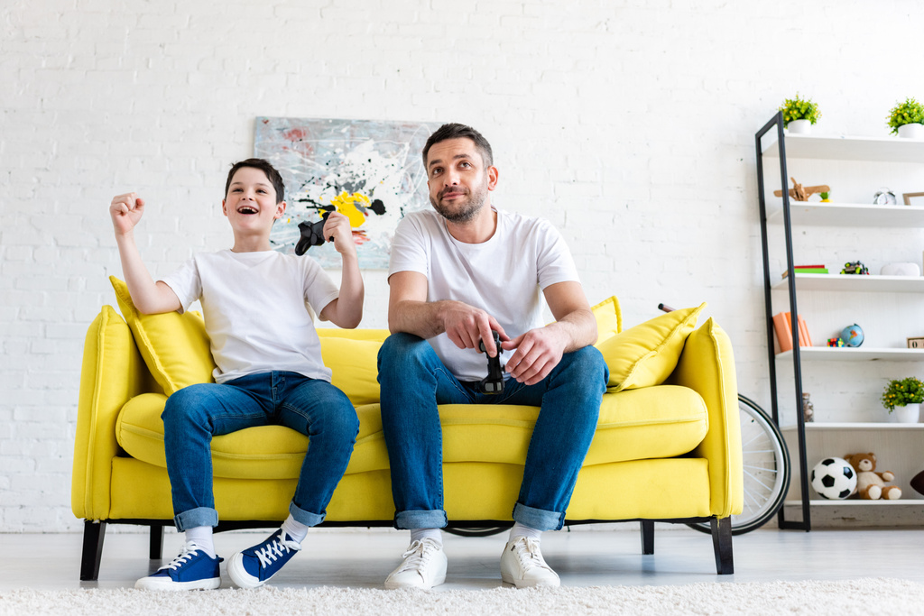 взволнованный сын болеет, играя в видеоигру с отцом на диване дома
 - Фото, изображение