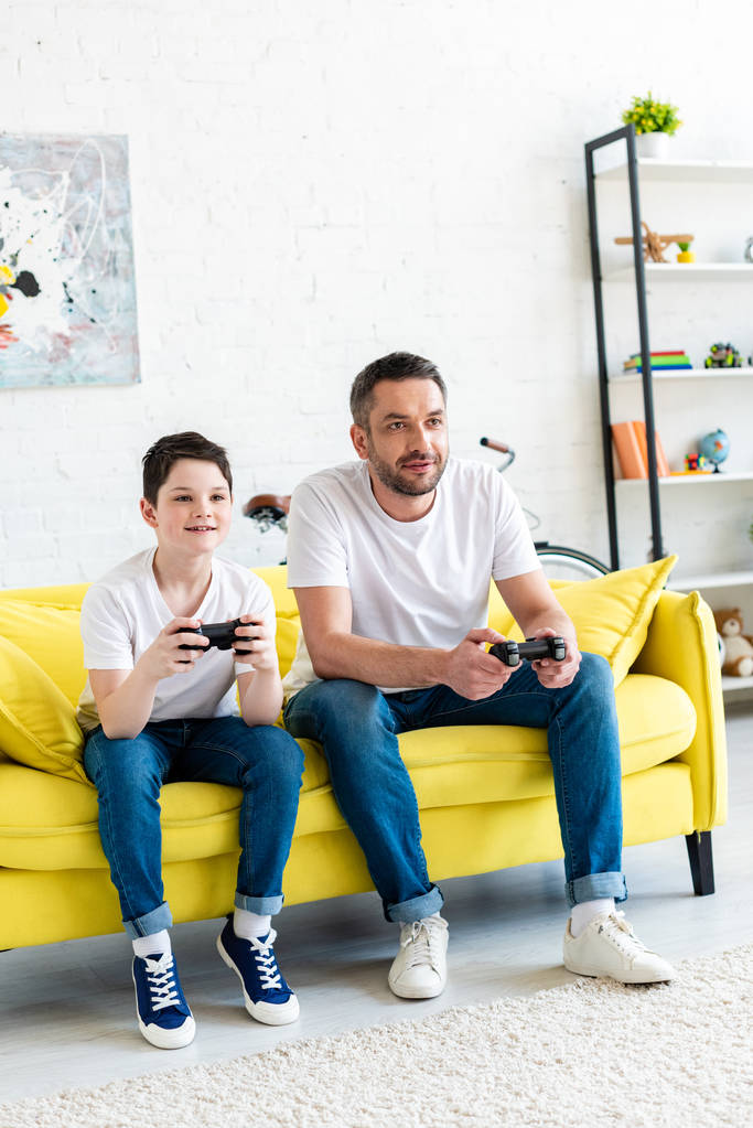 père et fils avec joysticks jouer au jeu vidéo sur le canapé dans le salon
 - Photo, image