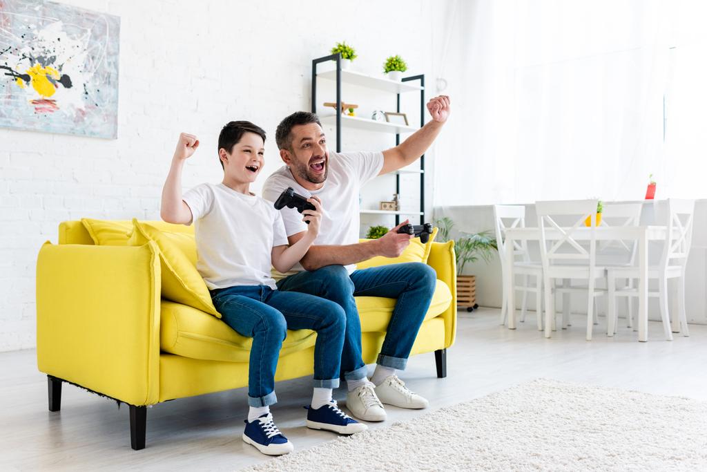 excité père et fils acclamant tout en jouant au jeu vidéo sur le canapé à la maison
 - Photo, image