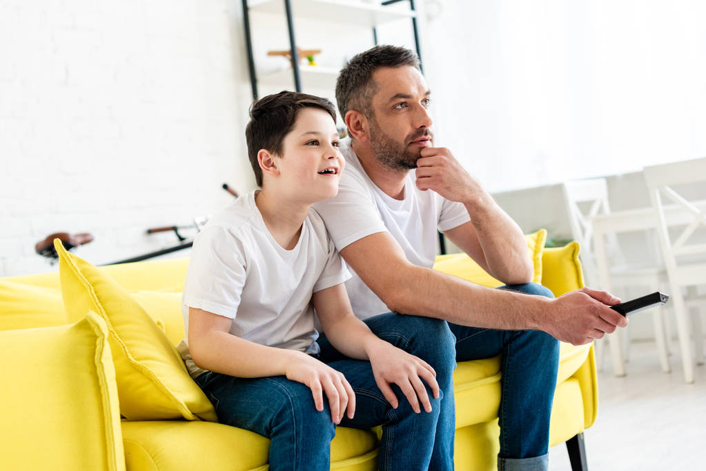 Isä ja poika istuvat sohvalla ja katsovat televisiota kotona
 - Valokuva, kuva