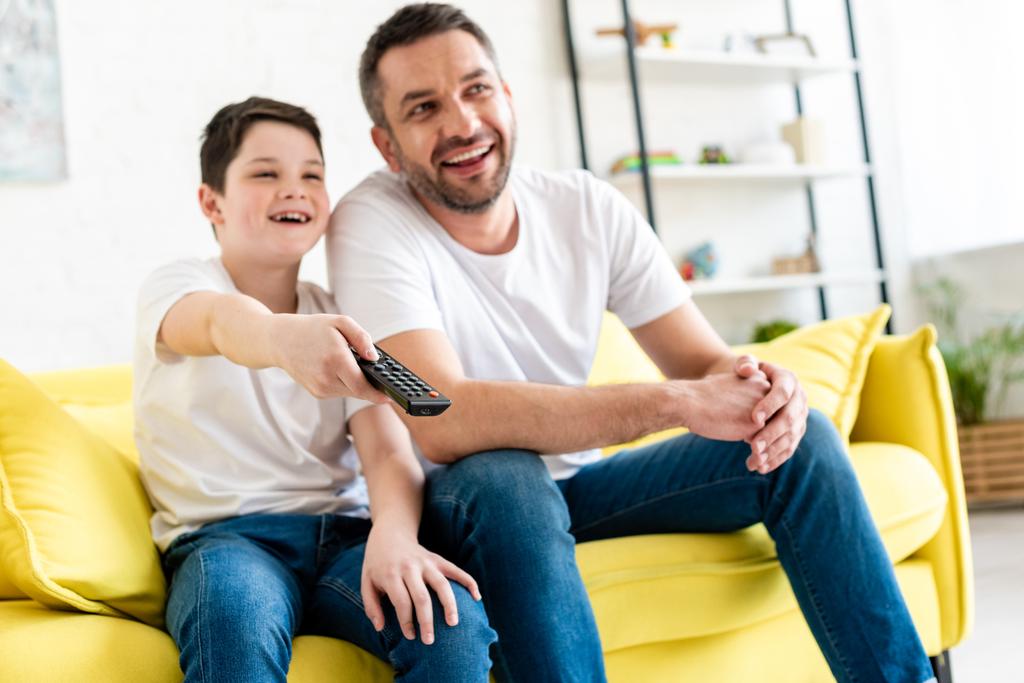 enfoque selectivo de feliz padre e hijo sentado en el sofá y viendo la televisión en casa
 - Foto, Imagen