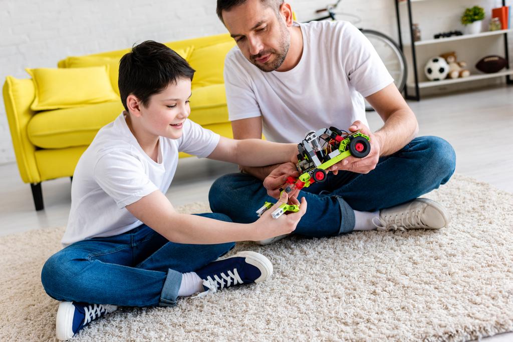 Vater und Sohn sitzen auf Teppich und spielen zu Hause mit Spielzeugauto - Foto, Bild