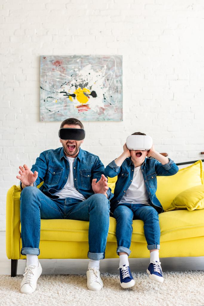 σοκ πατέρας και γιος σε VR ακουστικά βιώνουν εικονική πραγματικότητα στον καναπέ στο σπίτι - Φωτογραφία, εικόνα