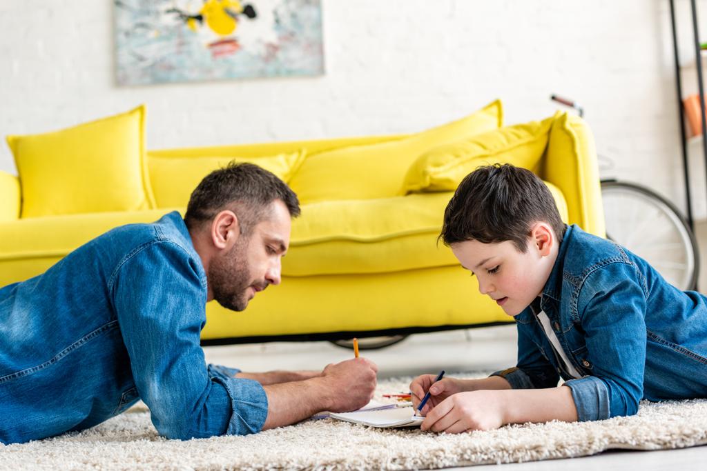 vader en zoon liggend op tapijt en tekening in de woonkamer - Foto, afbeelding