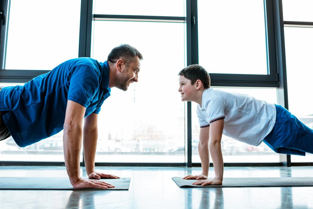 vader en zoon kijken naar elkaar terwijl het doen push up oefening in Gym - Foto, afbeelding