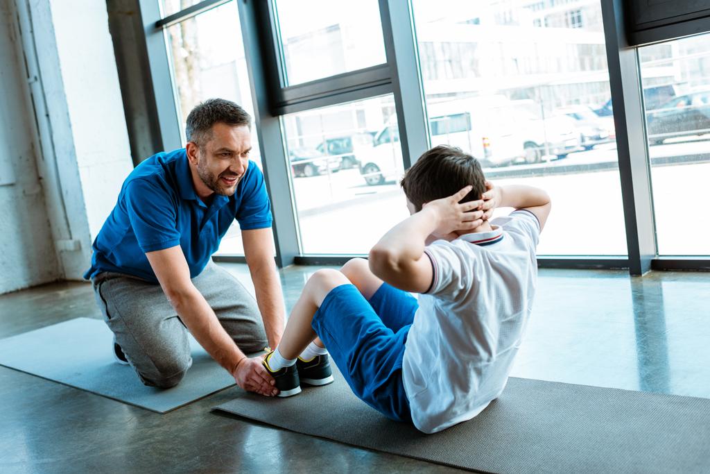 father helping son with sit up exercise at gym - Photo, Image