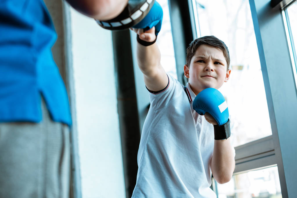 επιλεκτική εστίαση του αγοριού σε γάντια πυγμαχίας εκπαίδευση με προπονητή στο γυμναστήριο - Φωτογραφία, εικόνα