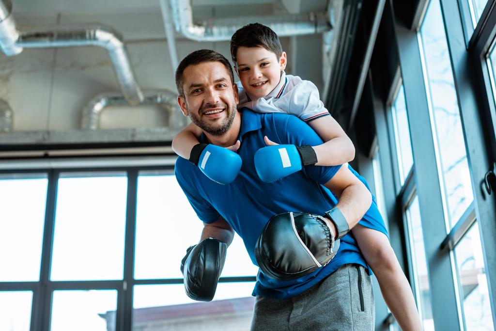 pai feliz dando passeio de piggyback para filho feliz em luvas de boxe no ginásio
 - Foto, Imagem