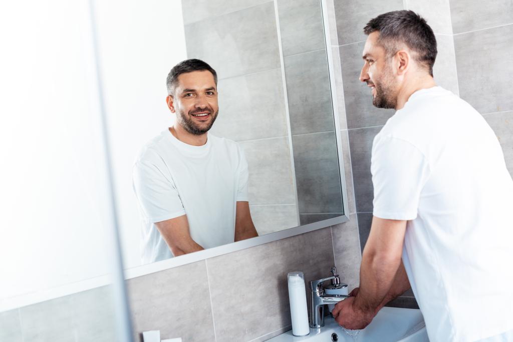 przystojny uśmiechnięty człowiek mycie rąk w łazience podczas porannej rutyny - Zdjęcie, obraz