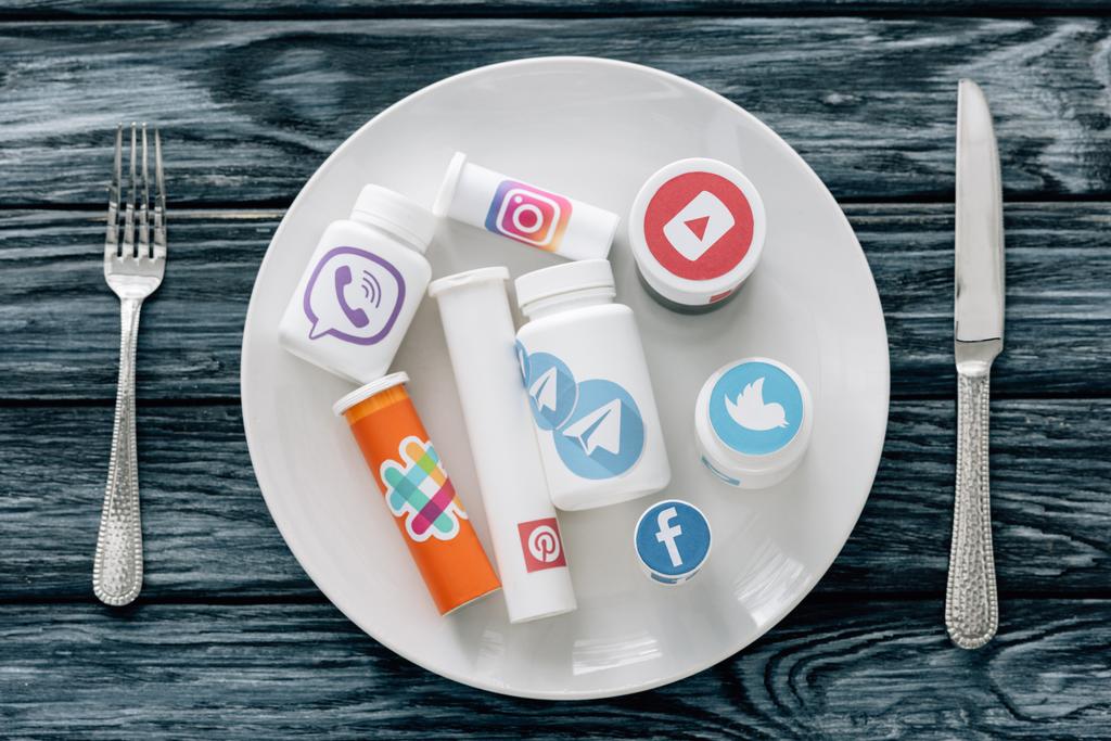 vista superior do recipiente com logotipos de mídia social na placa branca perto de faca e garfo na superfície de madeira cinza
 - Foto, Imagem