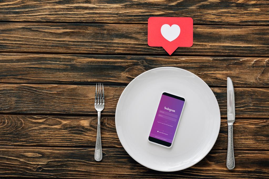 felső kilátás-ból smartphone-val Instagram app-ra képernyő közelében kést, Villa és a piros papír vágott kártya szív szimbóluma a barna fa felületén - Fotó, kép