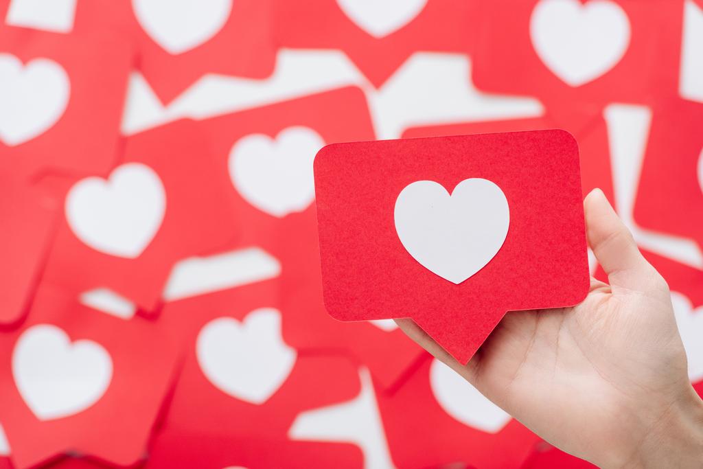 oříznutý pohled ženské ruky s červeným papírem střihanou kartou se symbolem srdce  - Fotografie, Obrázek