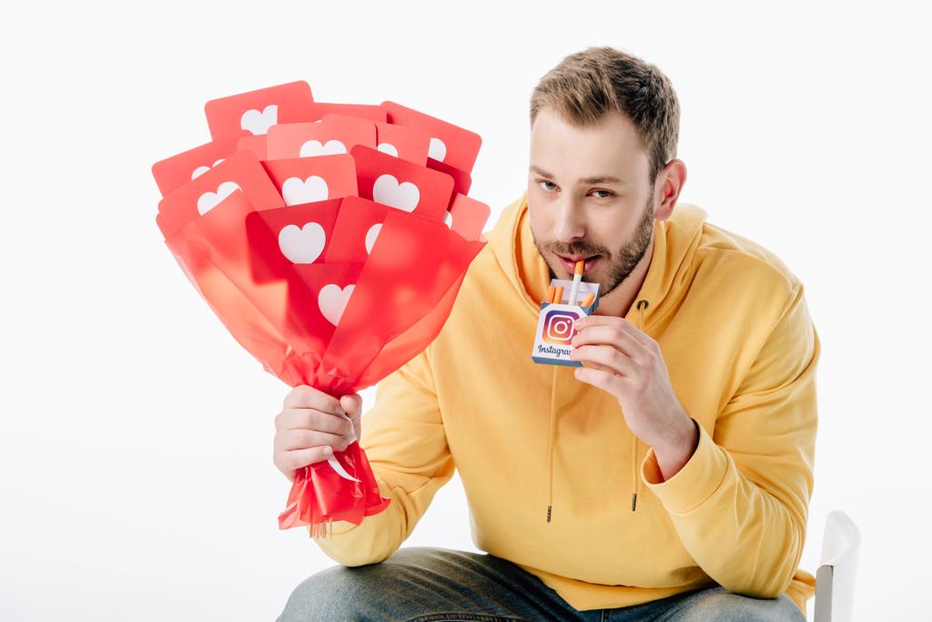 handsome man holding cigarette pack with instagram logo and bouquet of red paper cut cards with hearts symbols isolated on white - Photo, Image