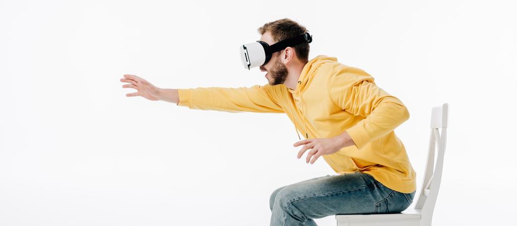 panoramatický záběr člověka, který roztahuje ruku při použití náhlavní soupravy pro virtuální realitu izolovaná na bílém - Fotografie, Obrázek