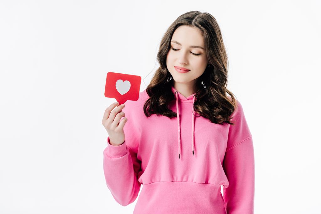 όμορφη νεαρή κοπέλα με ροζ κουκούλα κρατώντας κόκκινο χαρτί κοπής κάρτα με το σύμβολο της καρδιάς απομονώνονται σε λευκό - Φωτογραφία, εικόνα