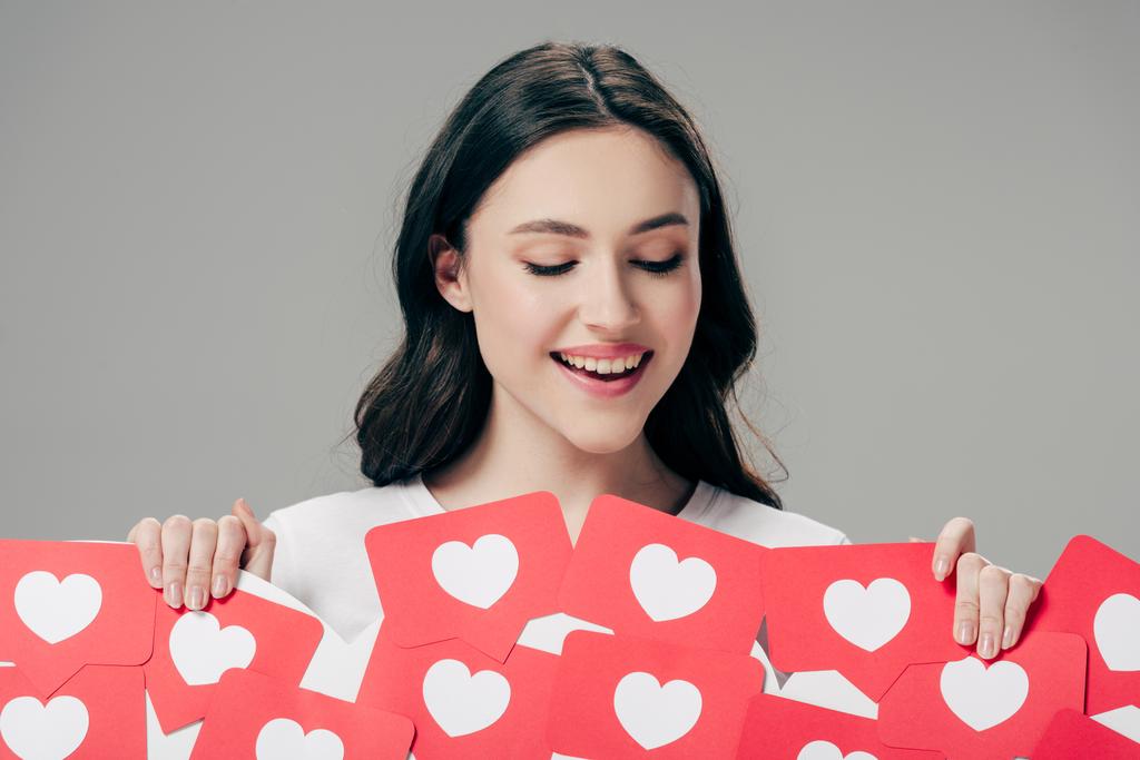 Pretty glimlachend meisje houdt rood papier knippen kaarten met harten symbolen geïsoleerd op grijs - Foto, afbeelding