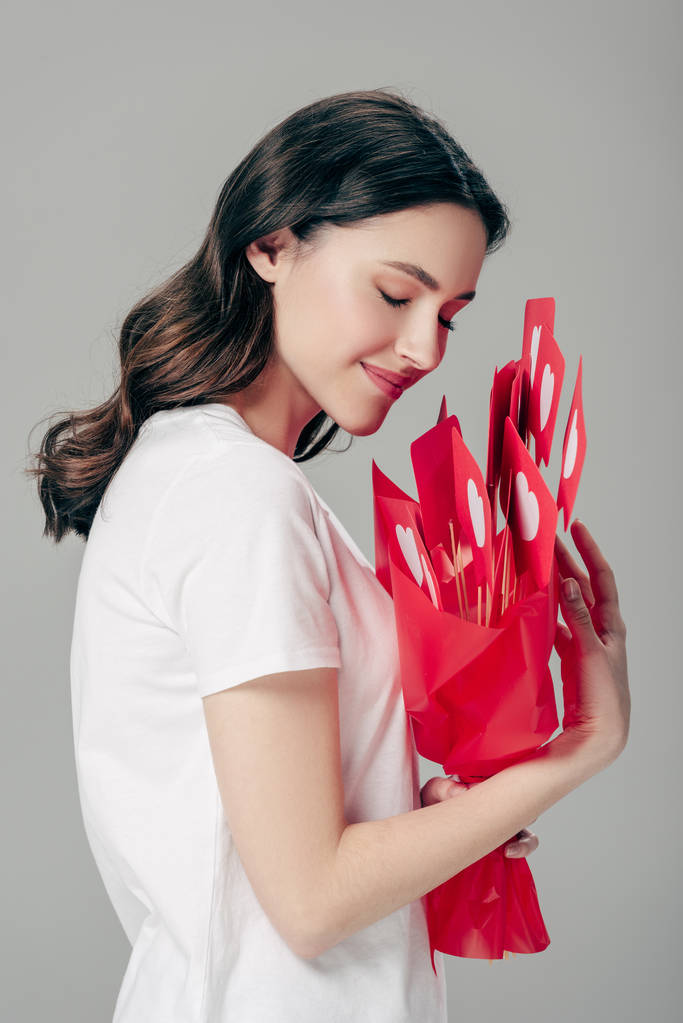 счастливая мечтательная девушка держит букет красной бумаги вырезанные карточки с символами сердца изолированы на сером
 - Фото, изображение