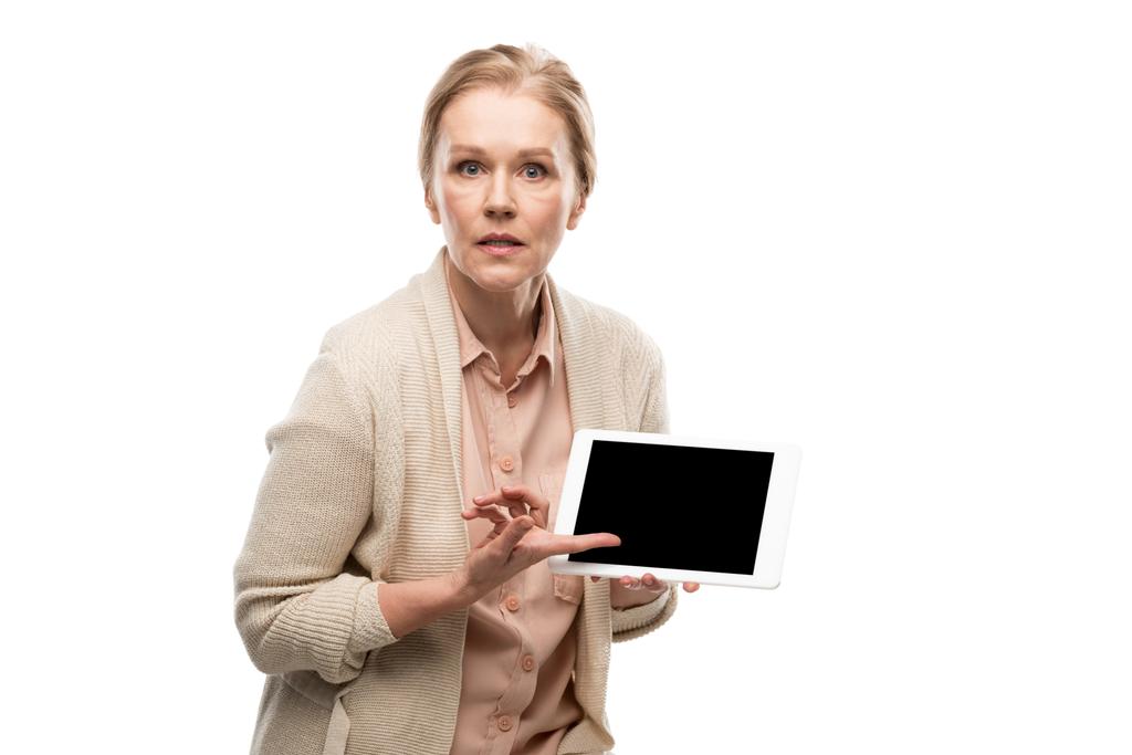 смущенная женщина средних лет, указывающая пальцем на цифровой планшет с пустым экраном, изолированным на белом
 - Фото, изображение