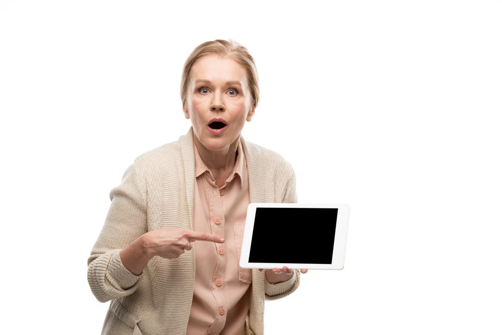 verrast middelbare leeftijd vrouw wijzend met de vinger op digitale tablet met blanco scherm geïsoleerd op wit - Foto, afbeelding