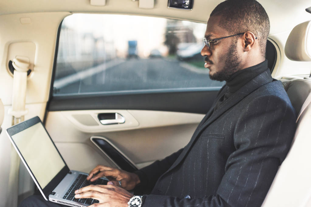 Homem em um terno de negócios escrever no laptop no salão de um carro caro com interior de couro
. - Foto, Imagem