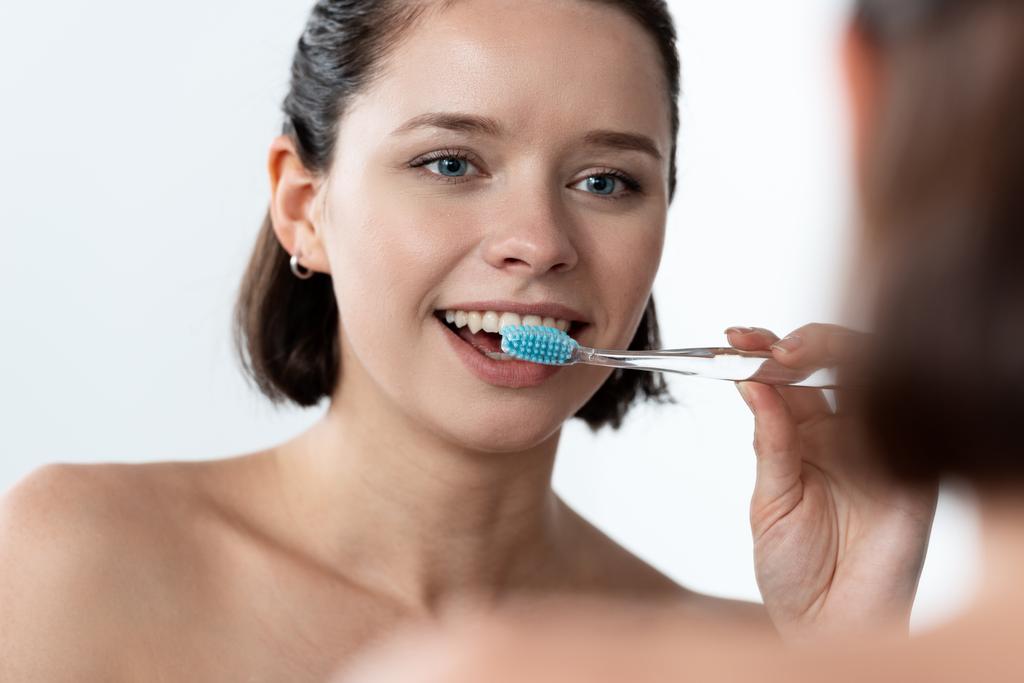 χαρούμενη νεαρή γυναίκα βουρτσίζει τα δόντια μπροστά από τον καθρέφτη - Φωτογραφία, εικόνα