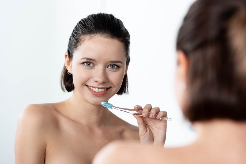 όμορφη χαμογελαστή κορίτσι κρατώντας οδοντόβουρτσα κοντά καθρέφτη στο μπάνιο - Φωτογραφία, εικόνα