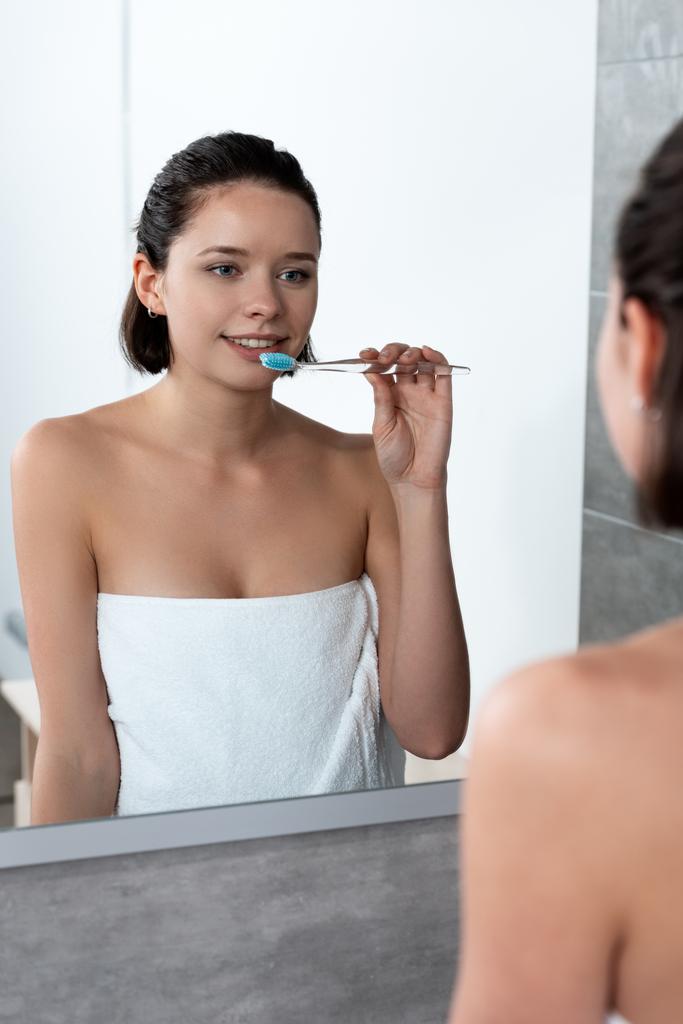 веселая женщина в полотенце чистить зубы перед зеркалом
 - Фото, изображение